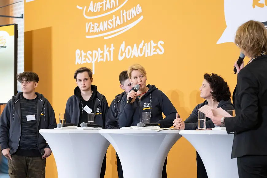 Das Bild zeigt Dr. Franziska Giffey, wie sie an Stehtischen mit Jugendlichen diskutiert