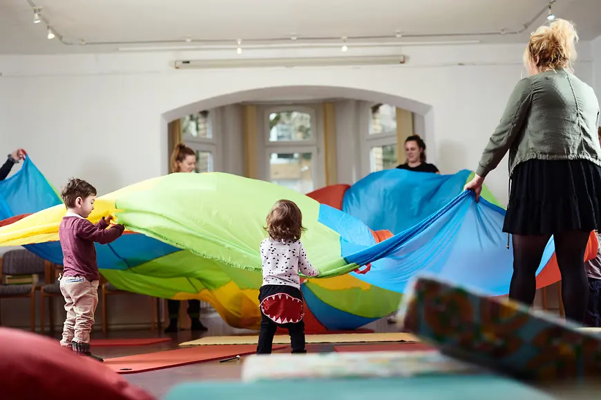Eine Gruppe von Kindern und Müttern spannt ein Tuch auf.
