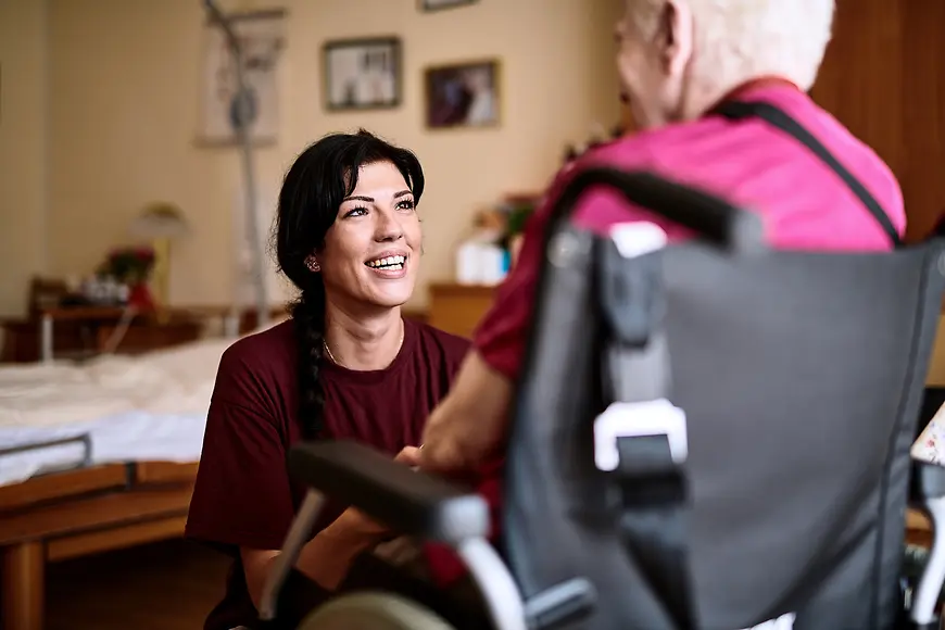Eine junge Frau kniet vor einer älteren Frau im Rollstuhl