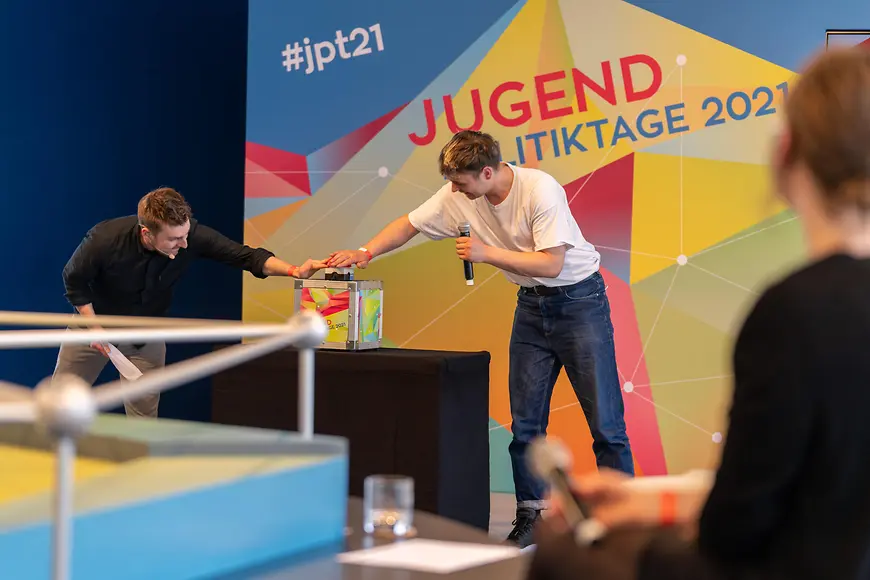 Zwei junge Menschen drücken bei den JugendPolititkTagen auf eine Button und starten das Online-Voting