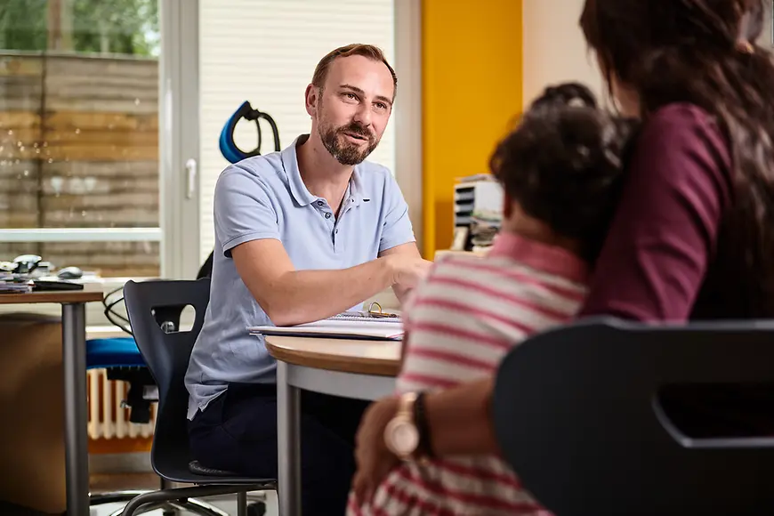 Ein junger Elternbegleiter erklärt einer Mutter mit Kind etwas
