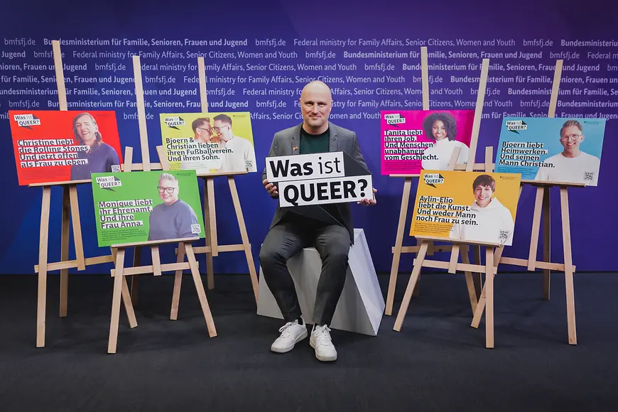 Sven Lehmann sitzt mit der Aufschrift "Was ist queer?" in den Händen umgeben von Plakaten mit den Kampagnenmotiven