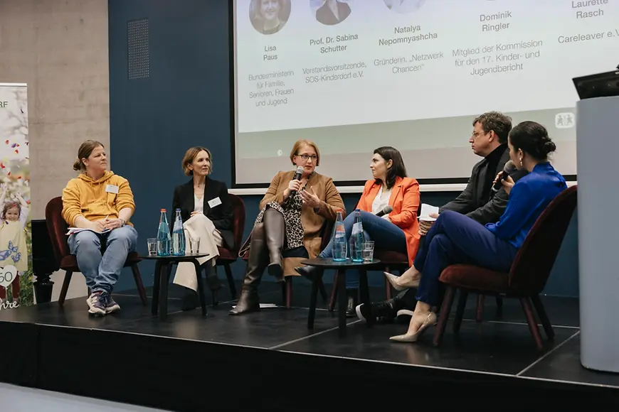 Lisa Paus sitzt mit einer Gruppe von Frauen auf einem Podium und hält ein Mikrofon