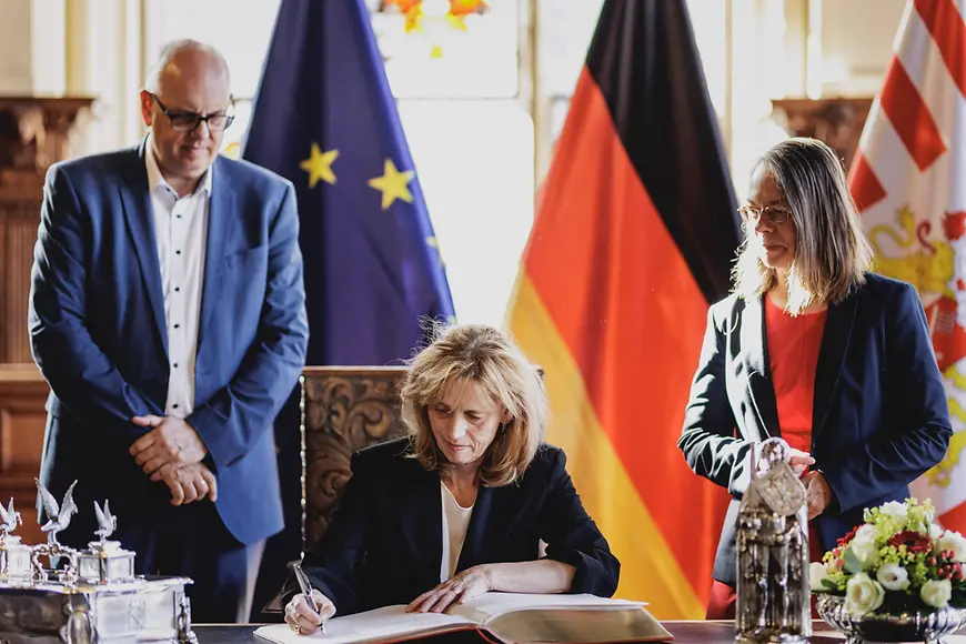 Karin Prien sitzt an einem Schreibtisch im Bremer Rathaus und trägt sich in ein Gästebuch ein