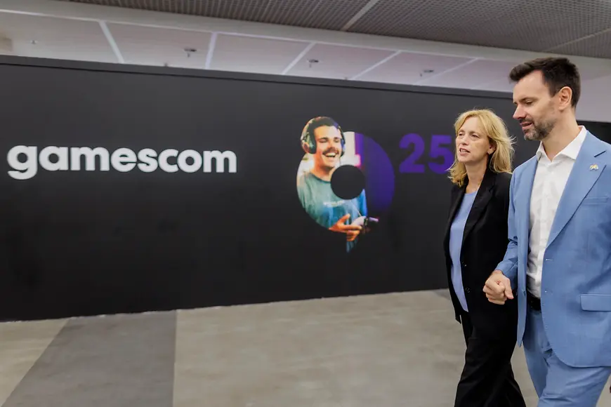 Karin Prien und Felix Falk laufen an einer Plakatwand vorbei auf der "Gamescom" steht