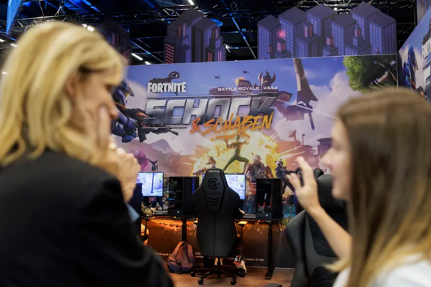 Eine große Plakatwand, auf der für ein Videospiel geworben wird, und vor der zwei Frauen stehen