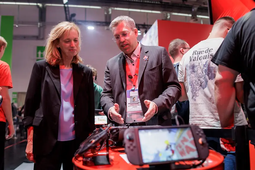 Karin Prien und Clemens Mayer-Wegelin stehen vor einem Tisch, auf dem Spielkonsolen liegen 