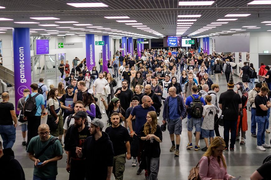 Besucherinnen und Besucher der Gamescom laufen einen großen Gang entlang
