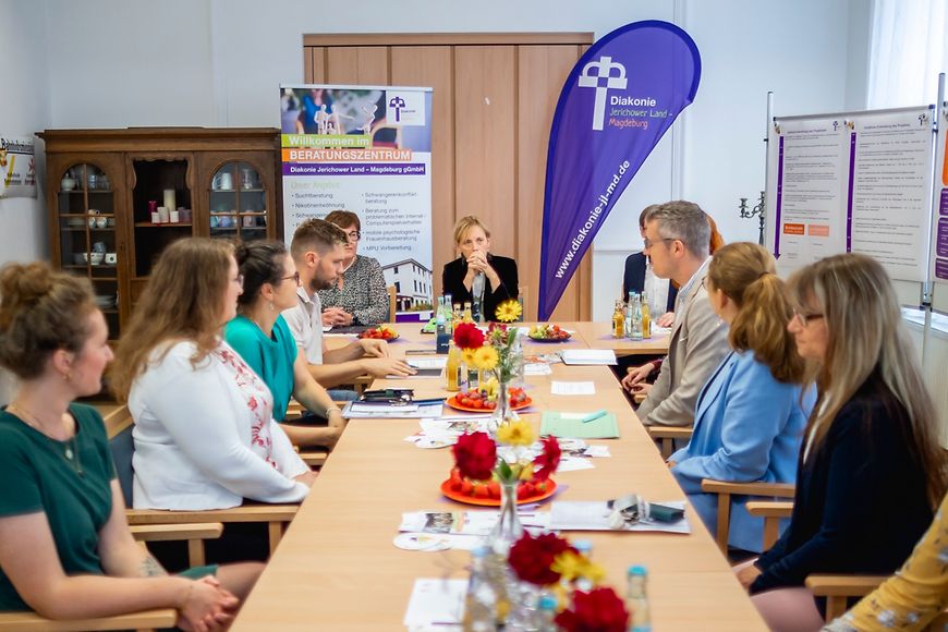 Karin Prien sitzt mit Vertreterinnen und Vertretern der Diakonie an einem großen Tisch