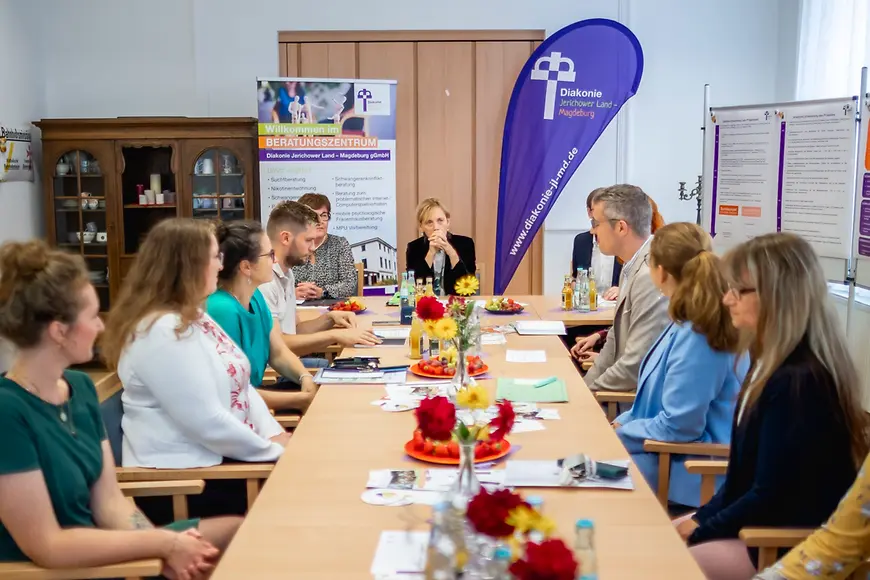 Karin Prien sitzt mit Vertreterinnen und Vertretern der Diakonie an einem großen Tisch