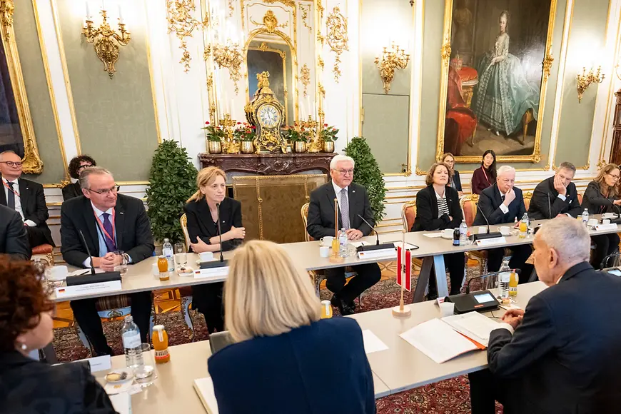 Frank-Walter Steinmeier und Karin Prien sitzen mit weiteren Personen an einem Tisch in einem Saal