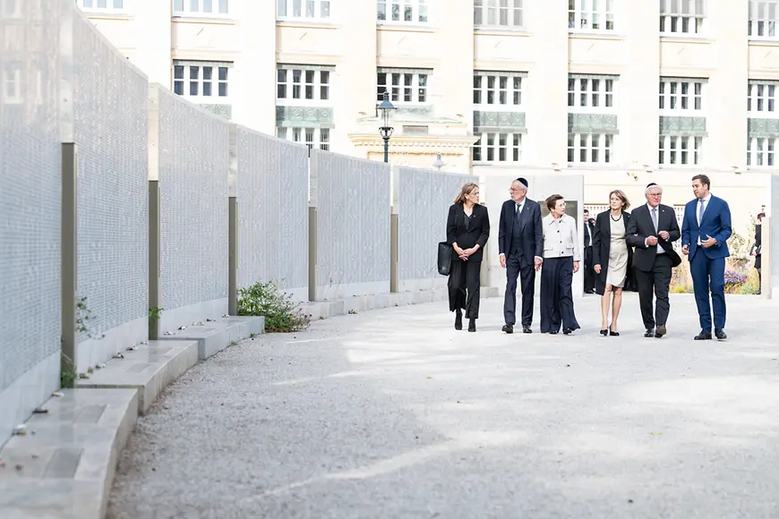 Frank-Walter Steinmeier und Karin Prien laufen mit weiteren Personen entlang der Gedänktafeln im Ostarrichi-Park