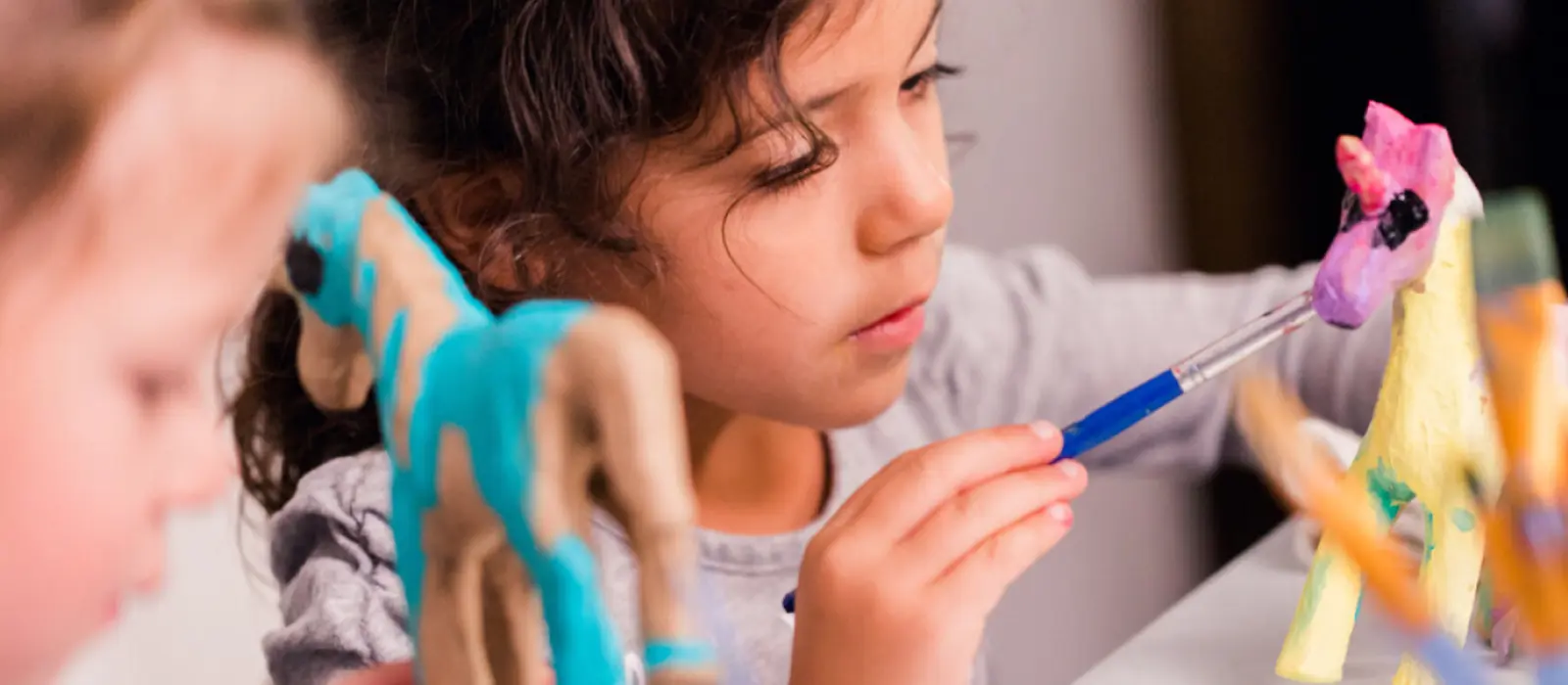 Zwei Kinder am Basteltisch bemalen Einhornfiguren mit bunten Farben.