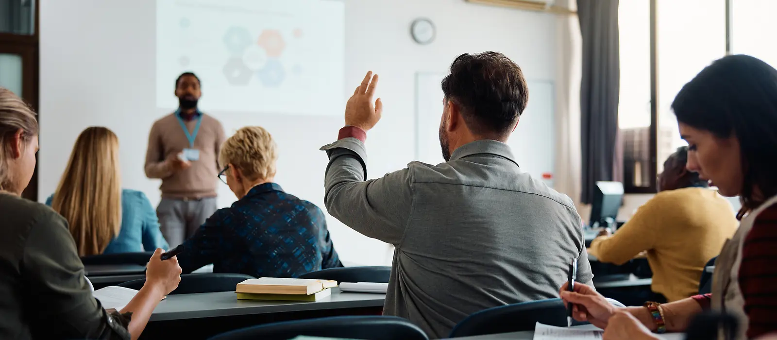 Ein Lehrer erklärt etwas vor einer Gruppe Erwachsener in einem Klassenraum.