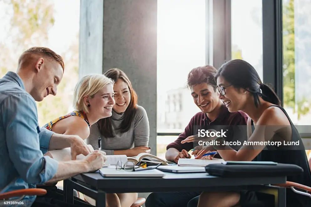Mehrere gut gelaunte Menschen sitzen in einem hellen Raum gemeinsam an einem Tisch und arbeiten mit Büchern und Stiften.