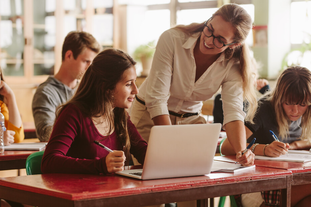 Eine Lehrerin erklärt lächelnd etwas am Laptop einer Schülerin