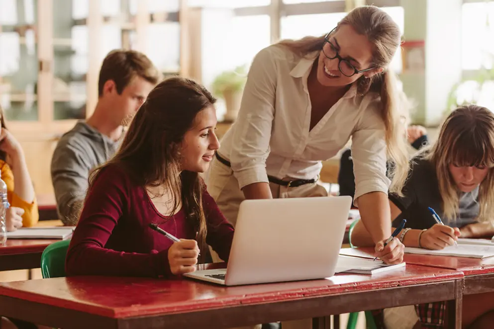 Eine Lehrerin erklärt lächelnd etwas am Laptop einer Schülerin