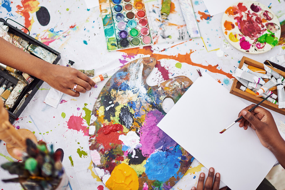 Eine Hand beim kreativen Arbeiten mit bunten Farben, Papier und Pinsel