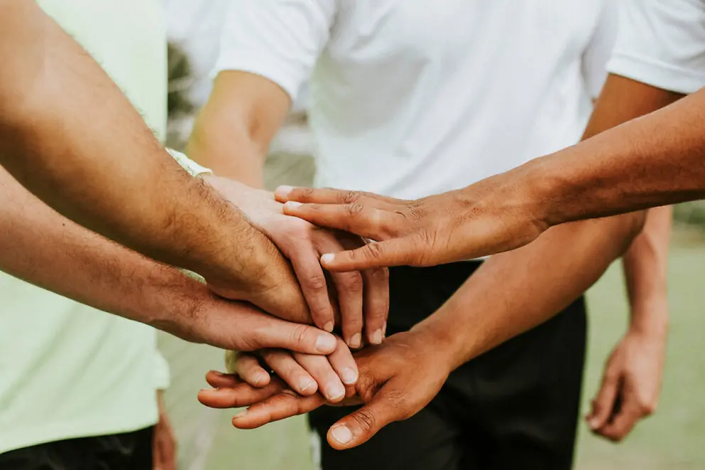 Mehrere übereinander gelegte Hände von verschiedenen Mensch, die symbolisch für Zusammenhalt stehen 