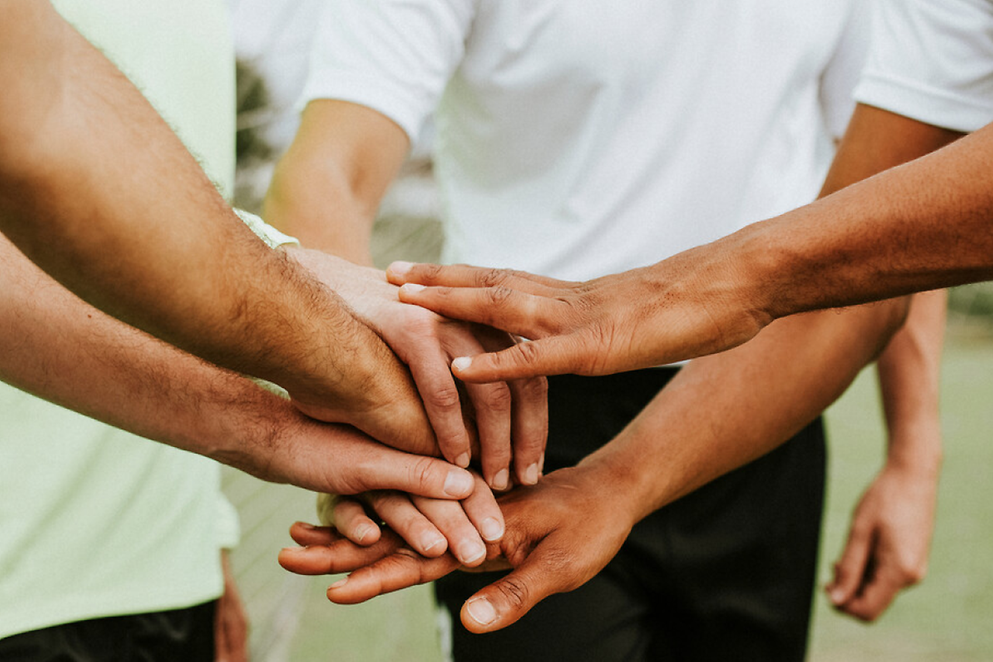 Mehrere übereinander gelegte Hände von verschiedenen Mensch, die symbolisch für Zusammenhalt stehen 