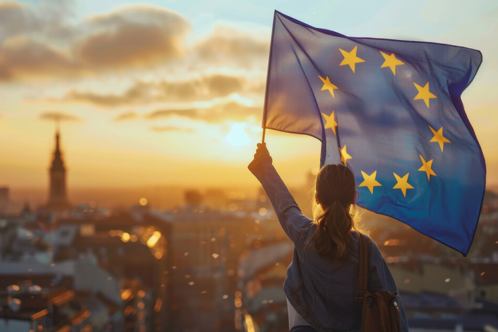 Eine Person mit langen Haaren schwenkt eine große EU-Flagge vor dem Panorama einer Stadt