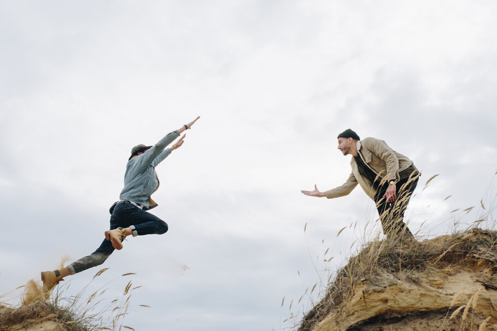 Zwei Personen stehen sich im Freien gegenüber. Eine Person springt der anderen schwungvoll entgegen. 