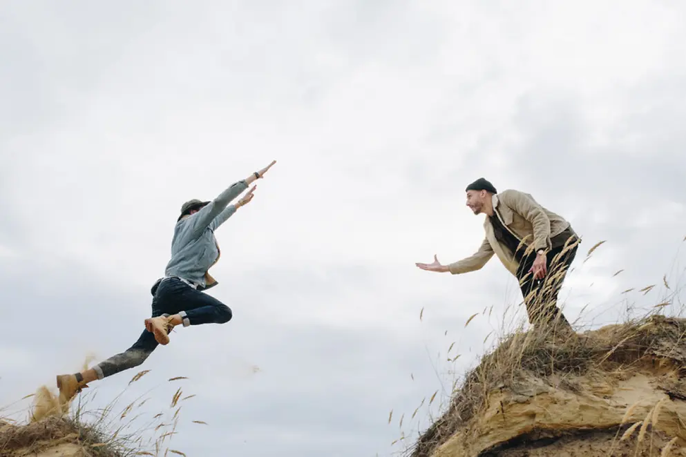 Zwei Personen stehen sich im Freien gegenüber. Eine Person springt der anderen schwungvoll entgegen. 