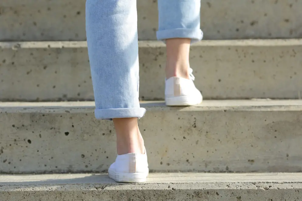 Eine Person in Jeans und weißen Sommerschuhen läuft eine Treppe in Beton-Optik hinauf 