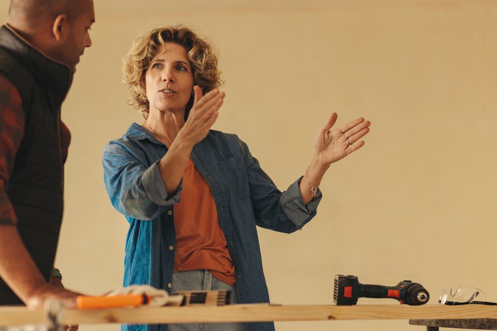 Eine Frau schaut zu einem Mann und erklärt ihm etwas, dabei hebt sie ihre Hände