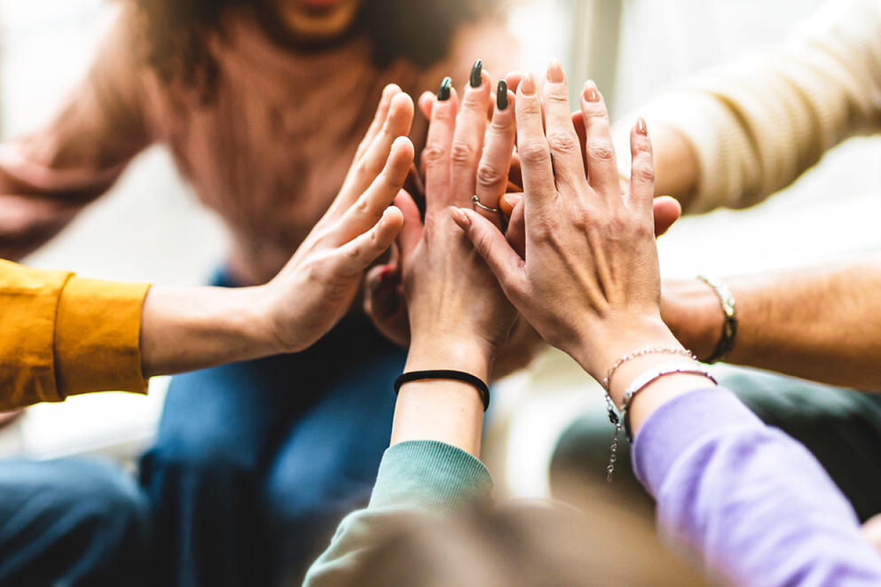 Mehrere Hände berühren sich in der Mitte eines Kreises und symbolisieren Verbundenheit