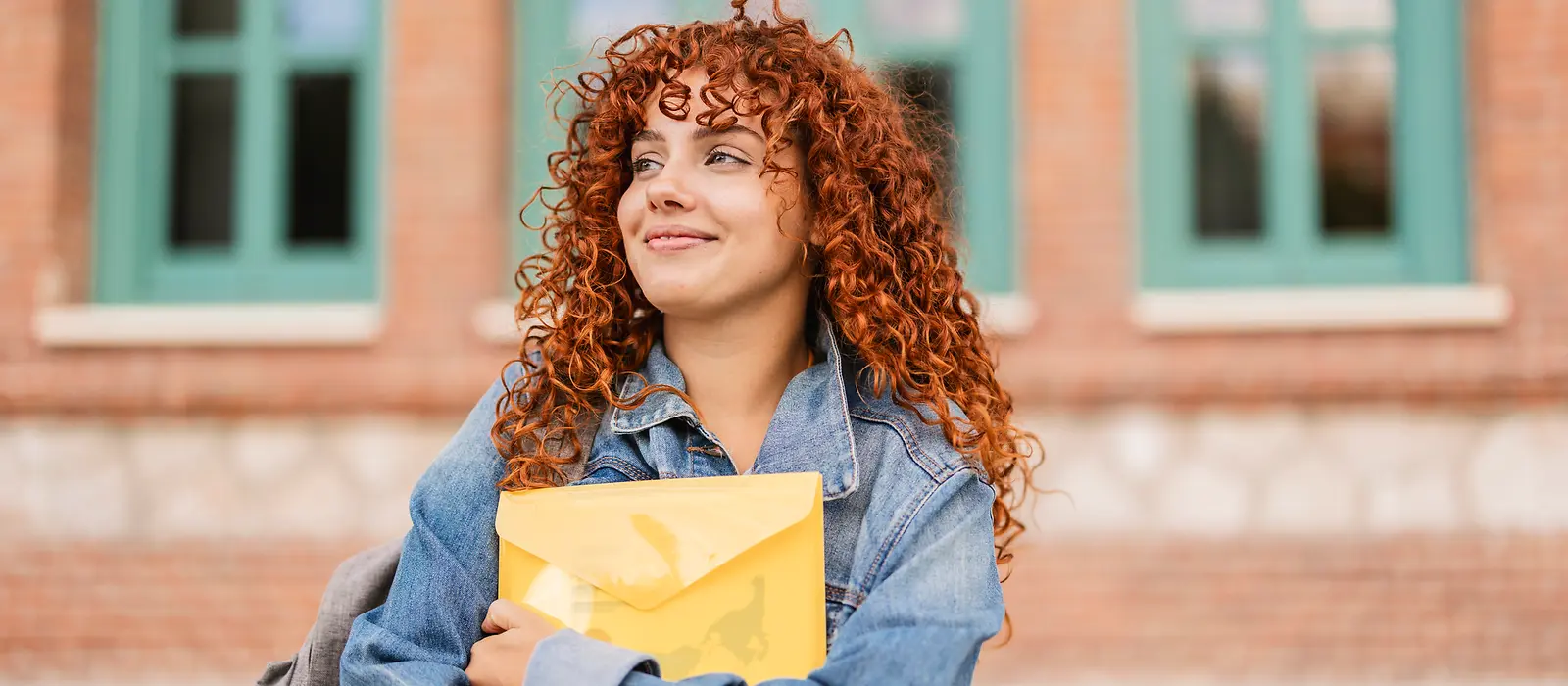 Eine Junge Frau hält eine gelbe Mappe mit Unterlagen und lächelt