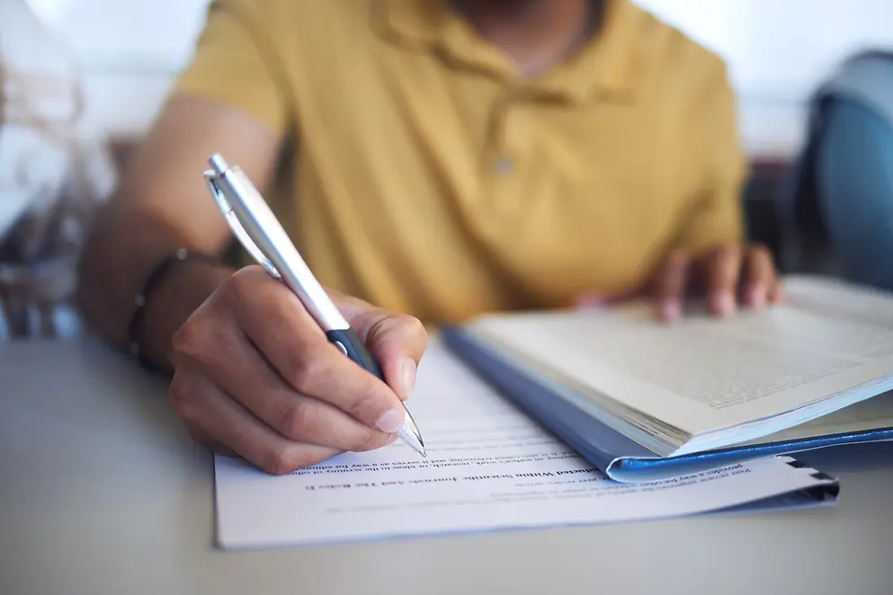 Eine Person sitzt an einem Tisch und schreibt etwas in Unterlagen