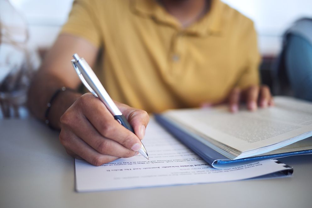 Eine Person sitzt an einem Tisch und schreibt etwas in Unterlagen