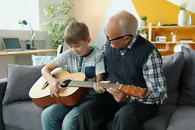 Ein älterer Mann spielt gemeinsam mit seinem Enkel Gitarre