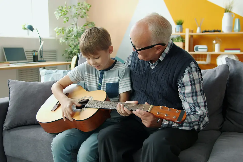 Ein älterer Mann spielt gemeinsam mit seinem Enkel Gitarre