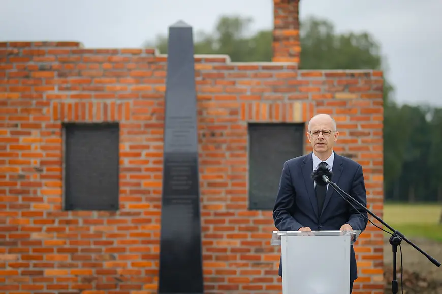 Michael Brand steht vor einem Rednerpult unter freiem Himmel vor einer Mauer
