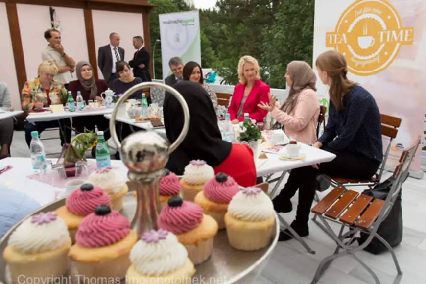 Manuela Schwesig sitzt mit den Teilnehmerinnen und Teilnehmern des Projekts "Tea Time" bei Kaffee und Kuchen an einem Tisch